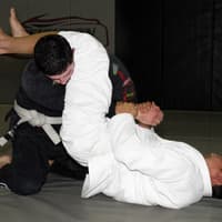 Two Brazilian Jiu-Jitsu practitioners at Creighton MMA engaged in a grappling exchange, with one attempting an armbar submission from the guard position.