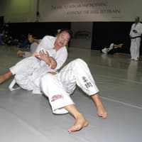 Two Brazilian Jiu-Jitsu practitioners at Creighton MMA engaged in a sparring session, with one executing an armbar submission while the other defends on the mat.