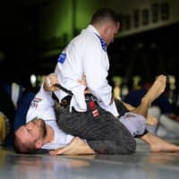 Two Brazilian Jiu-Jitsu practitioners at Creighton MMA engaged in a grappling exchange, with one attempting to maintain control while the other defends from the bottom position.