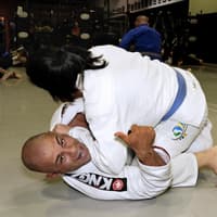 Two Brazilian Jiu-Jitsu practitioners sparring at Creighton MMA, with one giving a thumbs-up while defending from the bottom position in a gi.