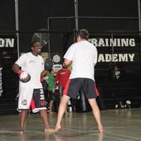 wo martial artists practicing striking drills with focus mitts at Creighton MMA Training Academy, with other students training in the background.