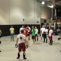 A group of martial artists in a kickboxing or MMA class at Creighton MMA Training Academy, standing in a circle listening to an instructor.