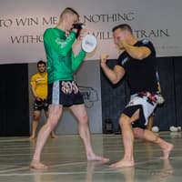 Paul Creighton demonstrating a striking technique, with teammates observing in the background.