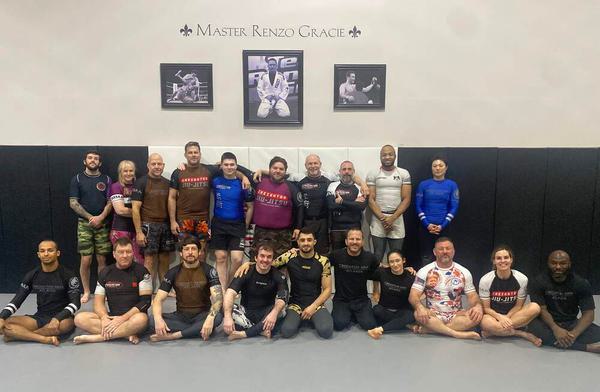 Creighton BJJ practitioners posing together on the mat at Creighton MMA under portraits of Master Renzo Gracie with Oliver Taza.